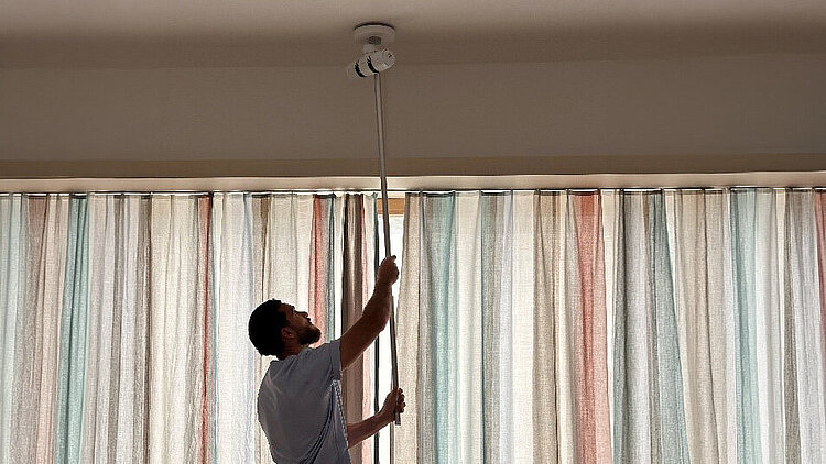 Ein Mann in Pfegekleidung hält einen Stab mit einem technischen Gerät nach oben, Richtung Decke.